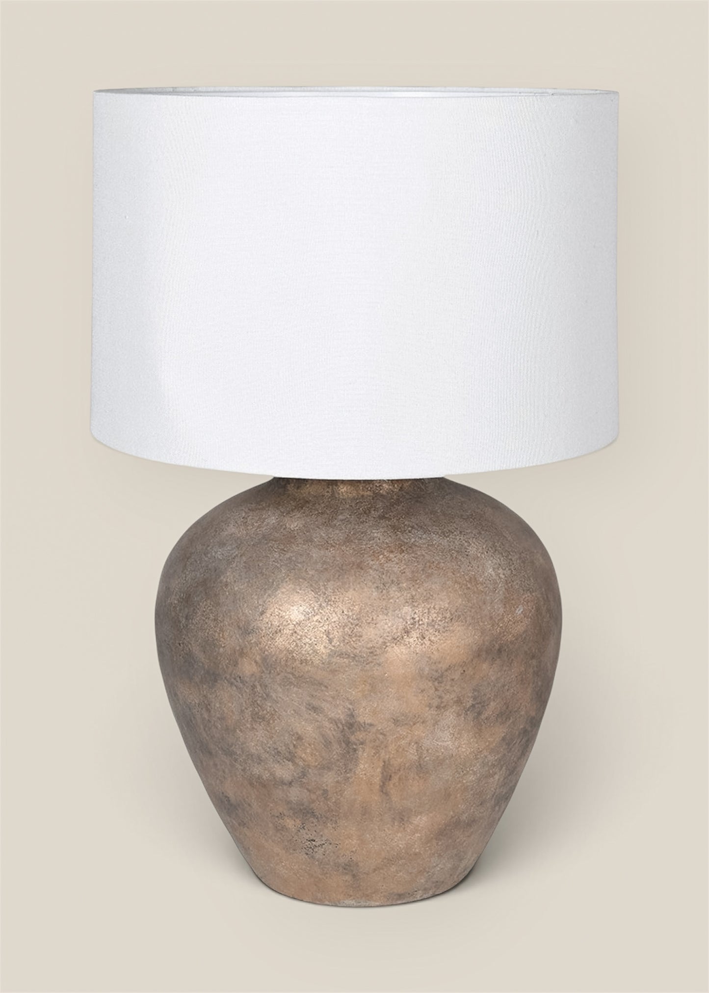 A table lamp with a textured metallic bronze base and a plain white drum shade