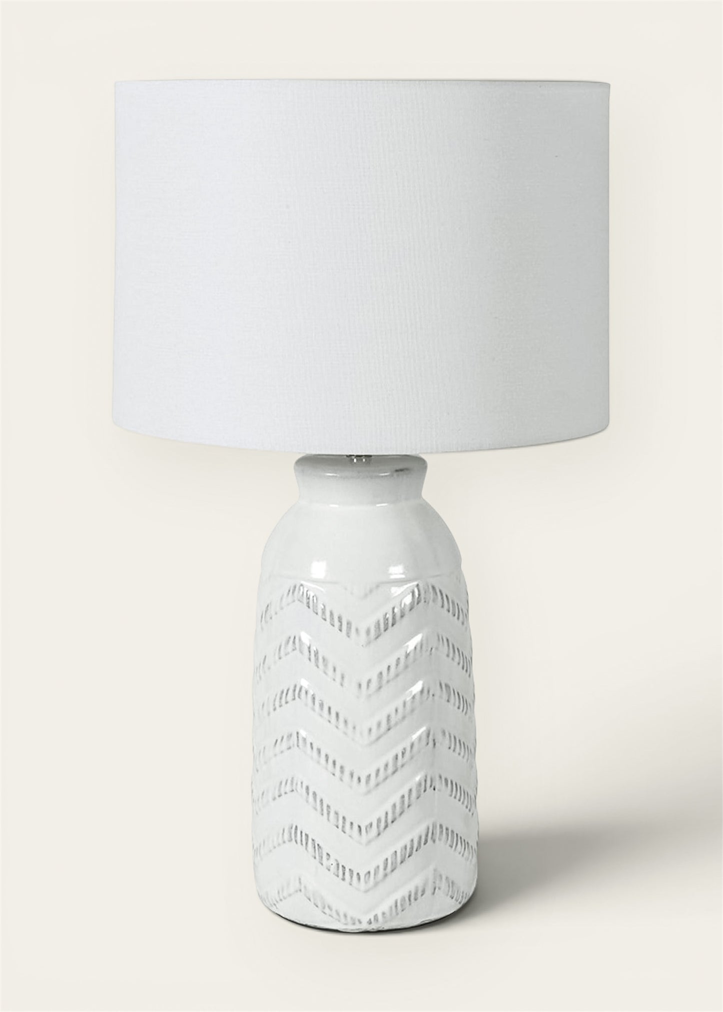 A modern table lamp with a textured white ceramic base featuring a geometric chevron pattern and a matching white drum shade.