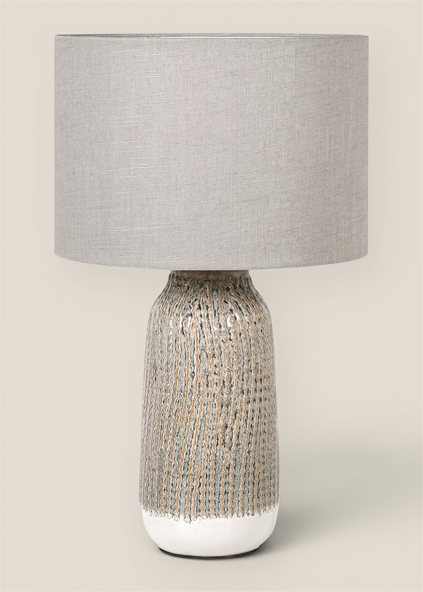 A table lamp with a textured ceramic base in beige tones with linen drum shade
