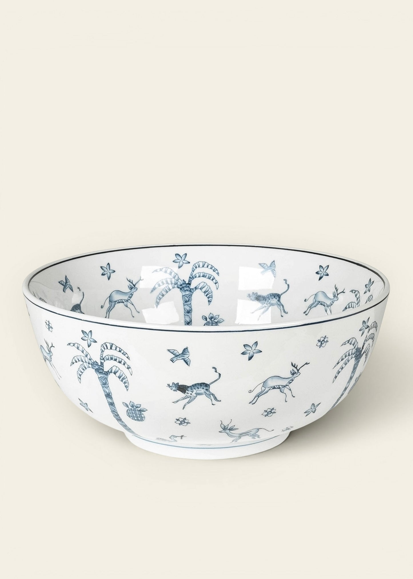 A white ceramic bowl decorated with a blue toile-style pattern of palm trees, birds, and butterflies