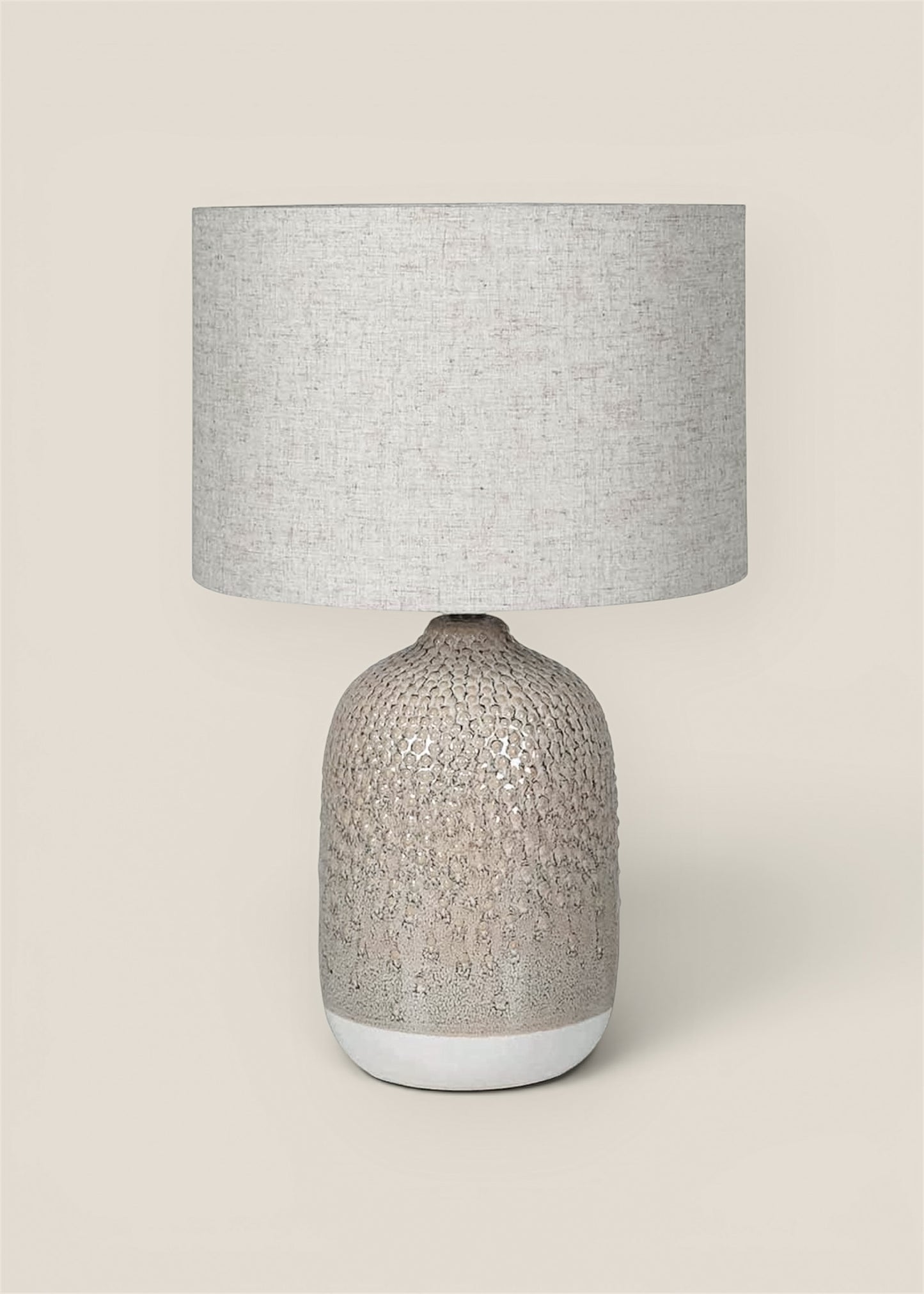 A table lamp with a textured, ceramic base and a linen drum shade