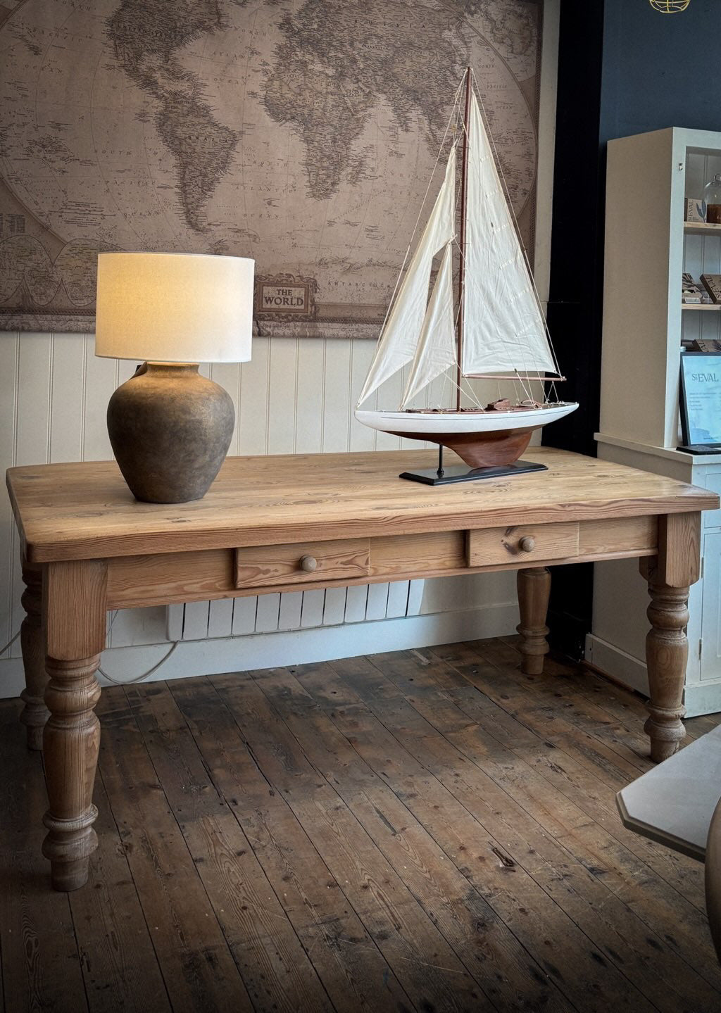 Wooden table with a lamp and model sailboat against a world map