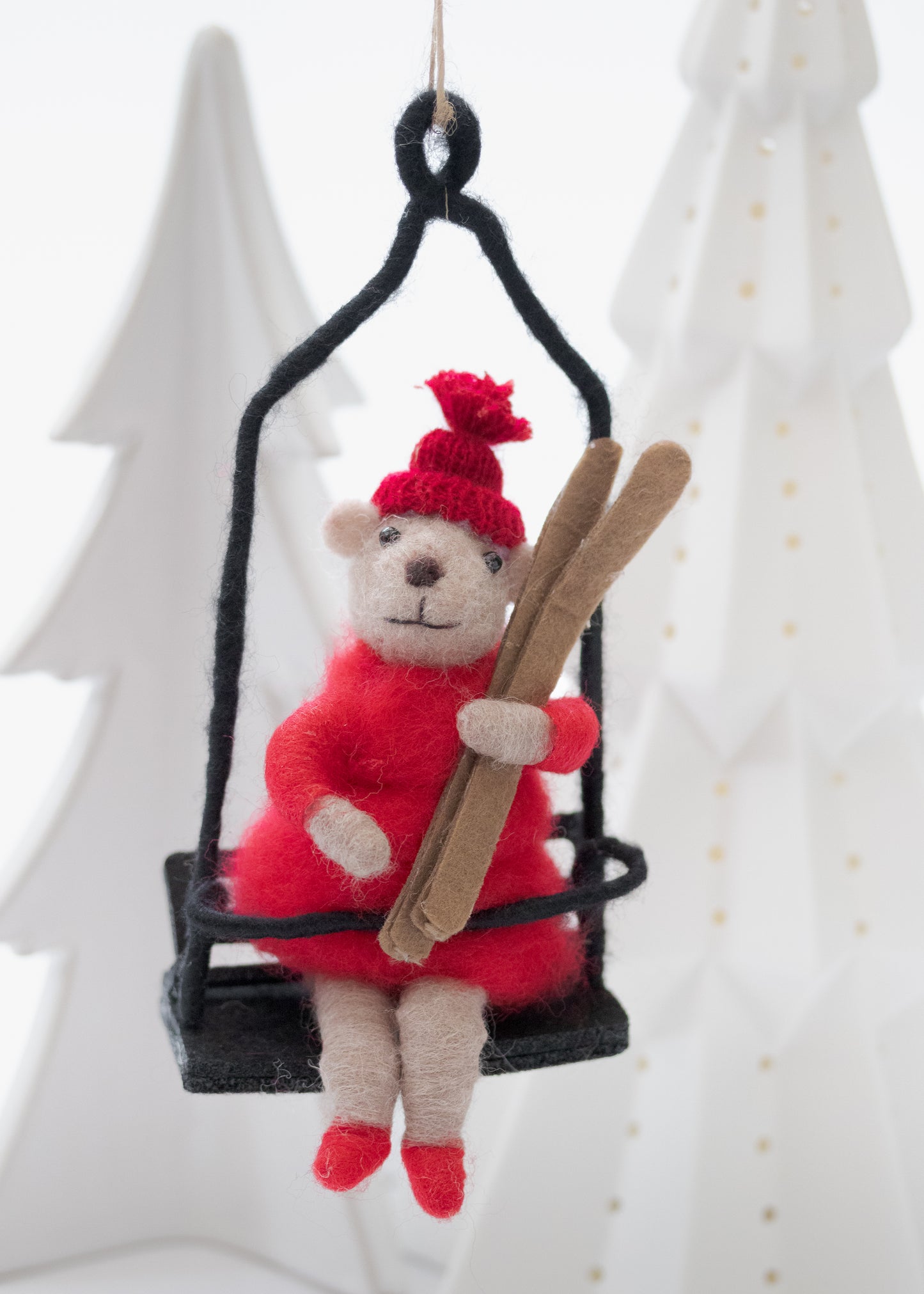 Decorative teddy bear ornament in a red outfit and hat, holding skis, on a black ski lift .