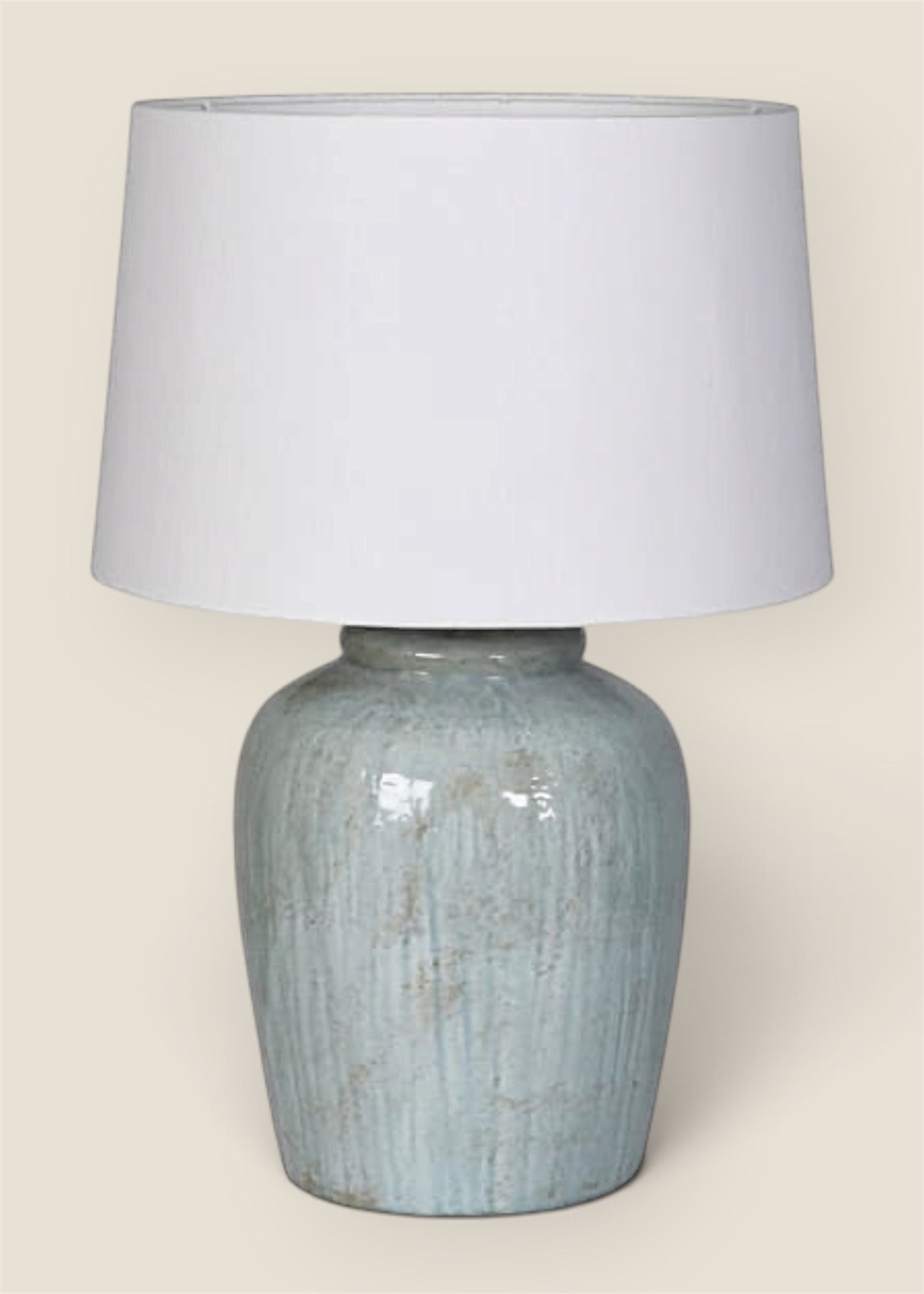 A table lamp with a textured, distressed light blue ceramic base and a large white fabric drum shade.